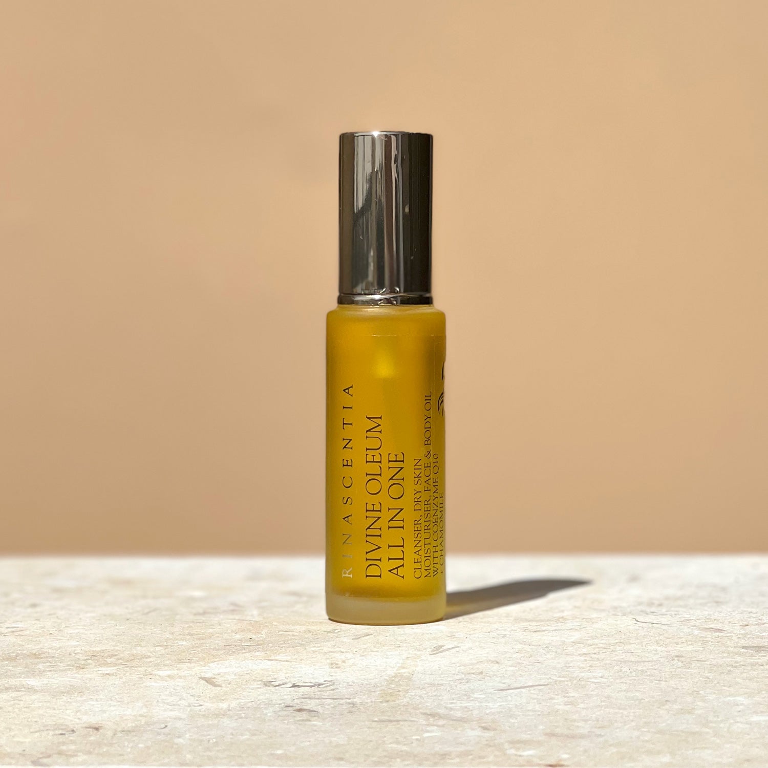 All in one cleansing oil serum in a bottle with gold lid on limestone base